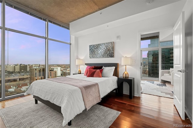 bedroom with a wall of windows, access to outside, baseboards, hardwood / wood-style flooring, and a view of city