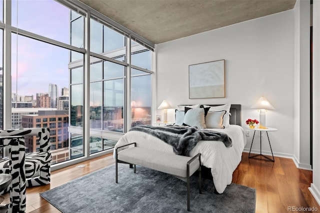 bedroom with baseboards, a city view, wood finished floors, and floor to ceiling windows