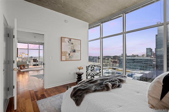 bedroom with a city view, floor to ceiling windows, wood finished floors, and baseboards