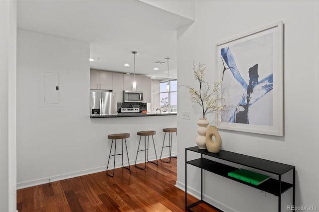 kitchen with dark wood-style floors, a breakfast bar, stainless steel appliances, dark countertops, and decorative light fixtures