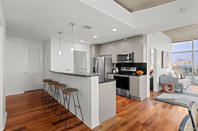 kitchen featuring a kitchen bar, wood finished floors, visible vents, and stainless steel appliances