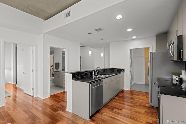 kitchen featuring dark countertops, visible vents, appliances with stainless steel finishes, a peninsula, and a sink