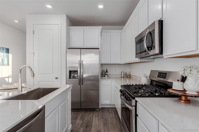 kitchen with stainless steel appliances, sink, light stone countertops, white cabinets, and dark hardwood / wood-style flooring