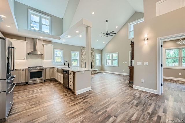 kitchen with high vaulted ceiling, stainless steel appliances, wood-type flooring, kitchen peninsula, and wall chimney exhaust hood