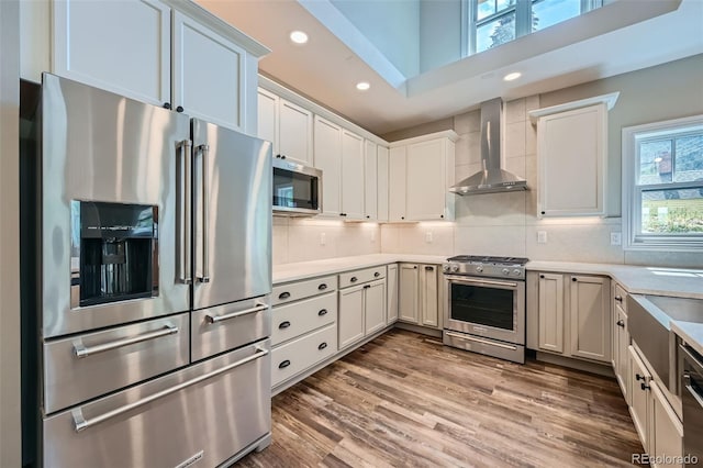 kitchen featuring wall chimney range hood, stainless steel appliances, white cabinetry, and a healthy amount of sunlight