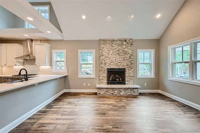 unfurnished living room featuring high vaulted ceiling, dark hardwood / wood-style flooring, and a stone fireplace