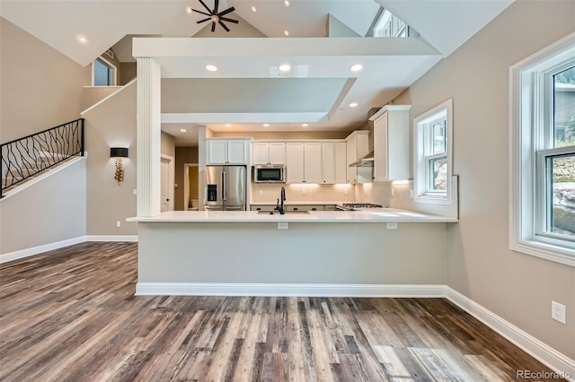 kitchen featuring wood-type flooring, kitchen peninsula, appliances with stainless steel finishes, and white cabinets