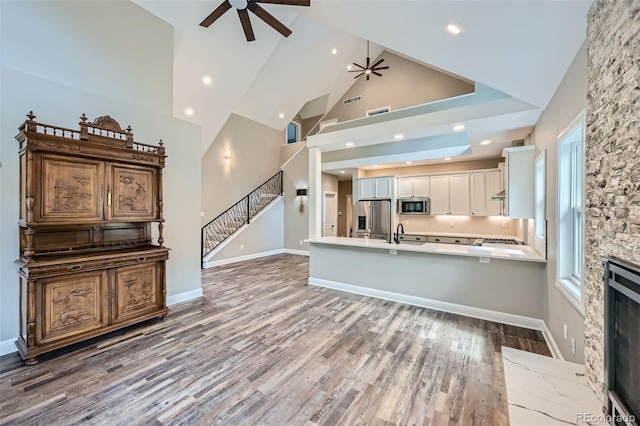 kitchen featuring a stone fireplace, stainless steel appliances, high vaulted ceiling, ceiling fan, and white cabinets