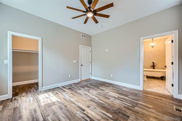 unfurnished bedroom featuring hardwood / wood-style floors, ceiling fan, a walk in closet, and ensuite bathroom