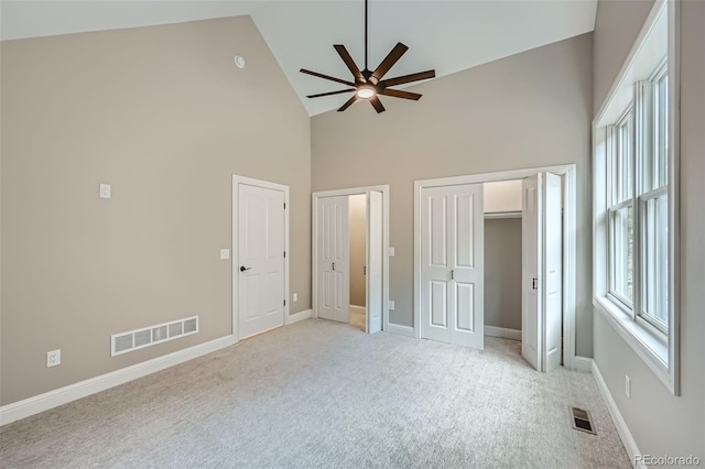 unfurnished bedroom featuring light colored carpet, high vaulted ceiling, two closets, and ceiling fan