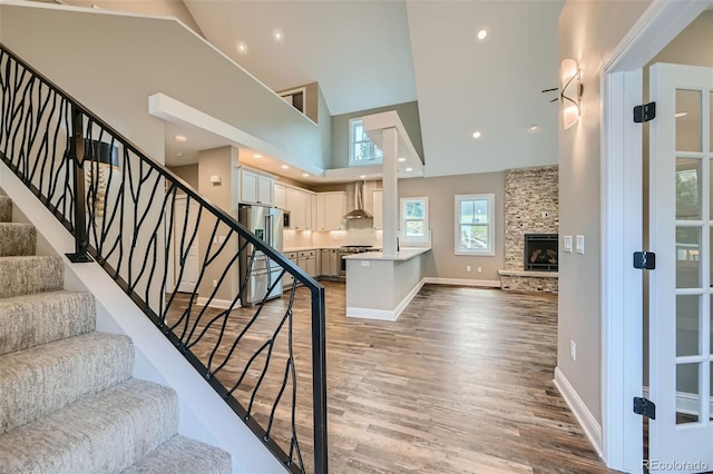 staircase featuring high vaulted ceiling, hardwood / wood-style flooring, and a fireplace