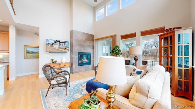 living area with visible vents, baseboards, light wood-type flooring, a fireplace, and a high ceiling