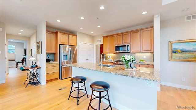 kitchen featuring tasteful backsplash, appliances with stainless steel finishes, light wood-type flooring, and a sink