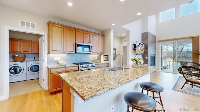 kitchen featuring light stone counters, visible vents, a sink, stainless steel appliances, and washing machine and dryer