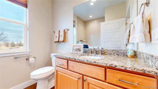 bathroom featuring toilet, plenty of natural light, vanity, and baseboards