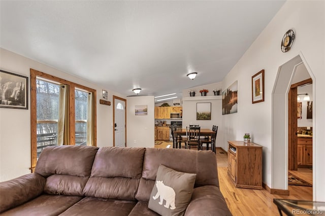 living area featuring light wood-style floors, baseboards, and arched walkways