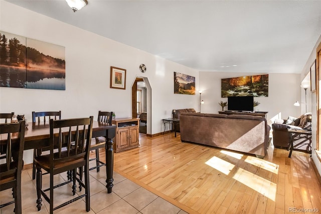 dining space with light wood-style floors, arched walkways, and baseboards