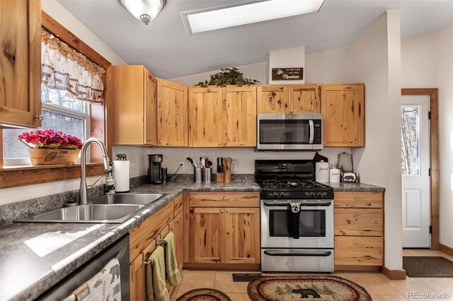 kitchen with light tile patterned floors, stainless steel appliances, dark countertops, vaulted ceiling, and a sink