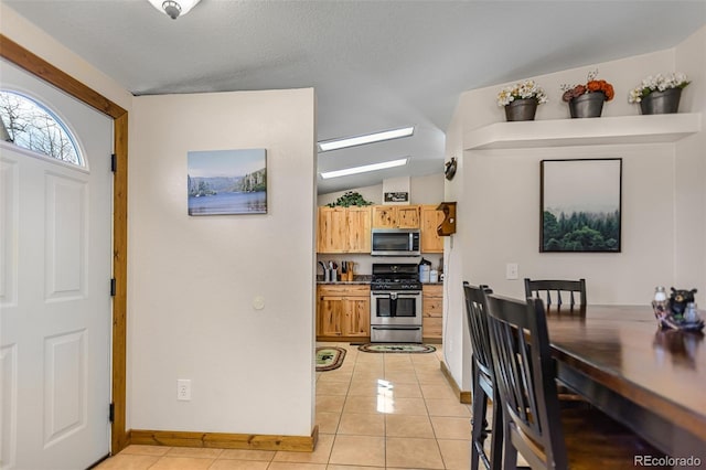 kitchen featuring light tile patterned floors, vaulted ceiling with skylight, a textured ceiling, baseboards, and appliances with stainless steel finishes