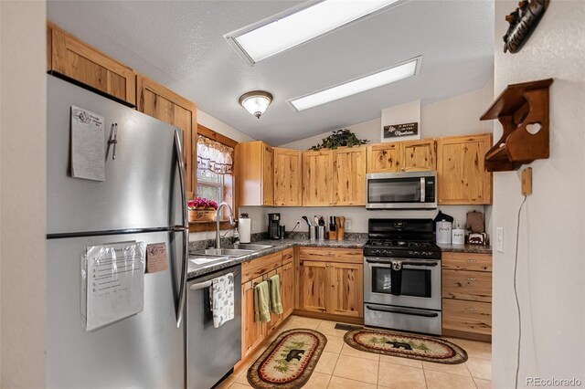 kitchen featuring lofted ceiling, light tile patterned flooring, stainless steel appliances, a sink, and dark countertops