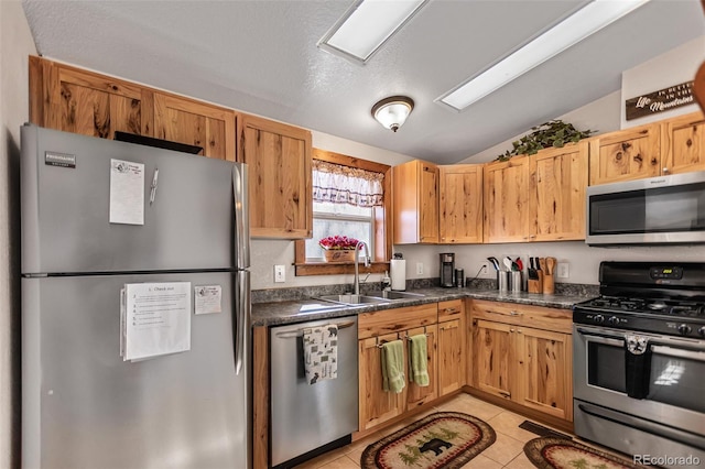 kitchen featuring appliances with stainless steel finishes, dark countertops, a sink, and light tile patterned floors