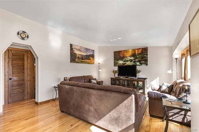 living area with arched walkways, baseboards, and light wood-style floors