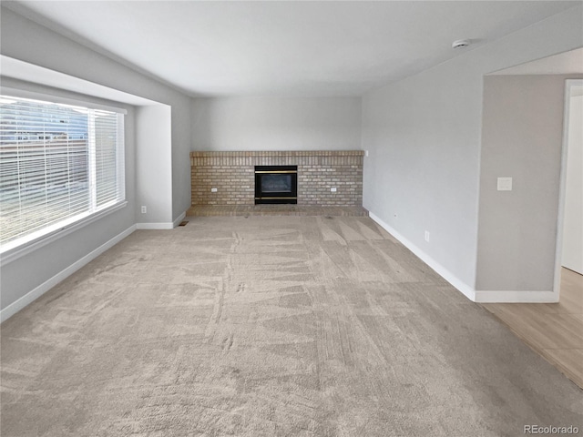 unfurnished living room featuring a brick fireplace, baseboards, and light colored carpet