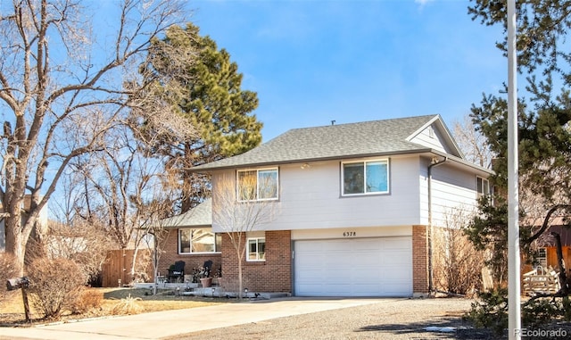 split level home featuring driveway, a shingled roof, an attached garage, fence, and brick siding