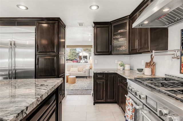 kitchen with visible vents, premium appliances, light stone countertops, extractor fan, and dark brown cabinets