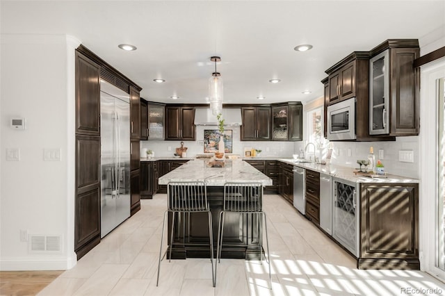 kitchen featuring stainless steel appliances, a kitchen island, visible vents, dark brown cabinets, and glass insert cabinets