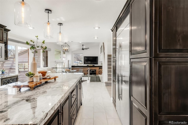 kitchen with dark brown cabinetry, ceiling fan, light stone counters, open floor plan, and hanging light fixtures