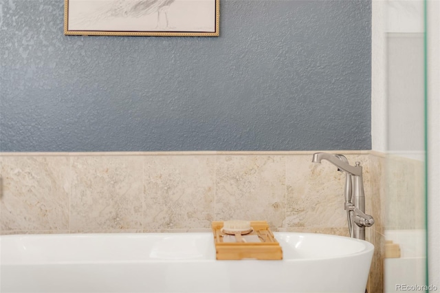 bathroom with a wainscoted wall, a textured wall, a soaking tub, and tile walls