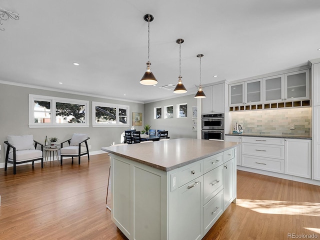 kitchen with white cabinetry, hanging light fixtures, decorative backsplash, a kitchen island, and double oven