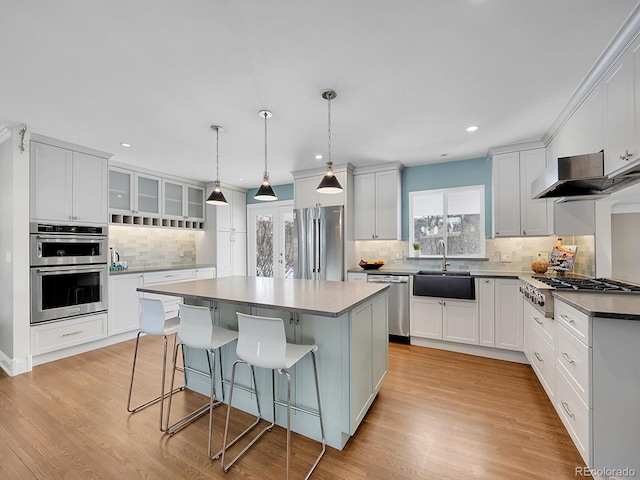 kitchen with appliances with stainless steel finishes, hanging light fixtures, white cabinets, a kitchen island, and sink