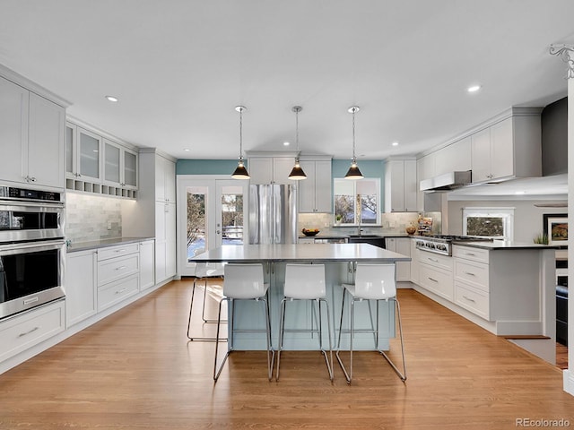 kitchen featuring a kitchen island, decorative light fixtures, stainless steel appliances, decorative backsplash, and light wood-type flooring