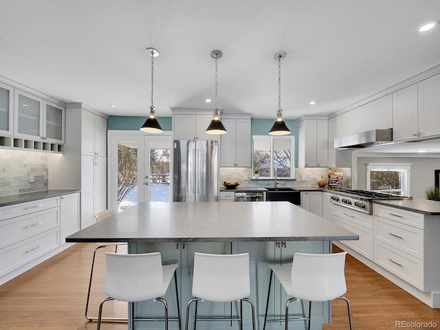 kitchen with pendant lighting, appliances with stainless steel finishes, extractor fan, tasteful backsplash, and a kitchen island