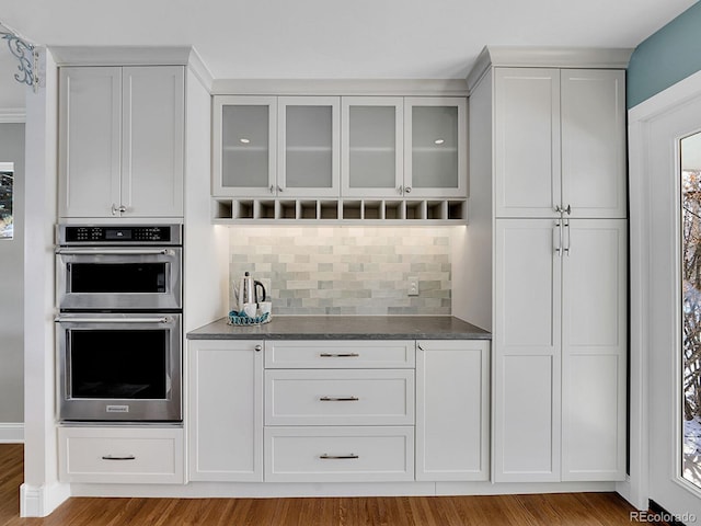 interior space with tasteful backsplash, white cabinets, dark stone countertops, light hardwood / wood-style flooring, and double oven