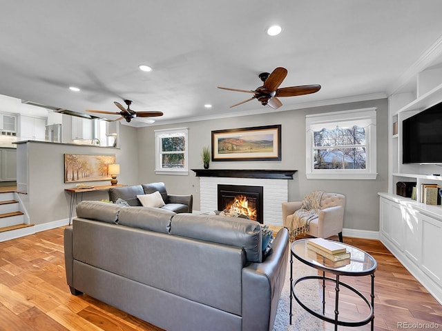 living room with ornamental molding, ceiling fan, a brick fireplace, and light hardwood / wood-style flooring