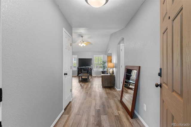hall with light wood-type flooring, baseboards, and a textured wall