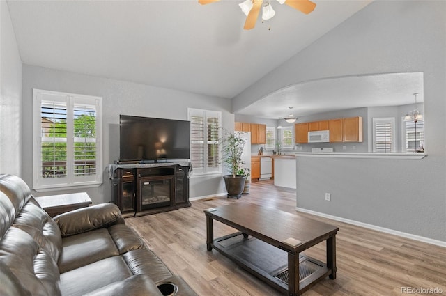 living area featuring ceiling fan, vaulted ceiling, light wood-style floors, and baseboards