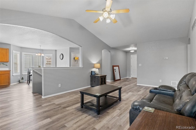 living area with arched walkways, a ceiling fan, vaulted ceiling, a chandelier, and light wood-style flooring