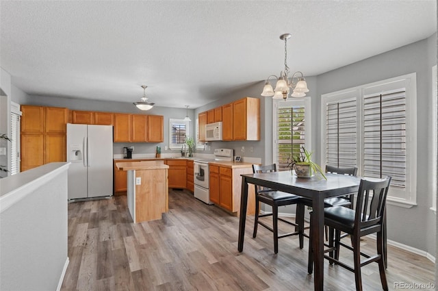 kitchen with white appliances, light countertops, a kitchen island, light wood finished floors, and a chandelier