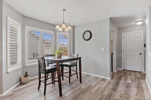 dining space with light wood-type flooring, a chandelier, baseboards, and a textured ceiling