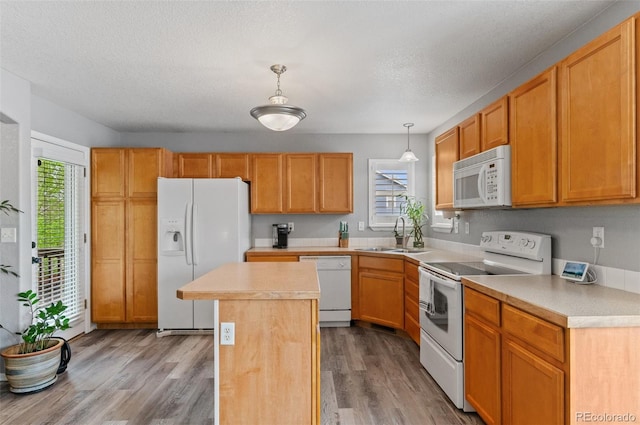 kitchen featuring white appliances, a sink, a center island, light countertops, and wood finished floors