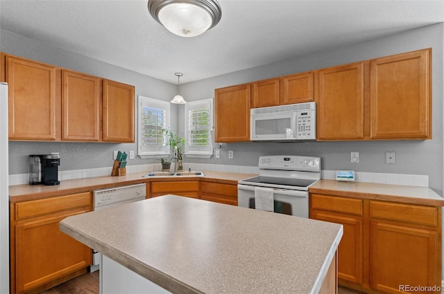 kitchen featuring white appliances, a sink, light countertops, a kitchen island, and decorative light fixtures