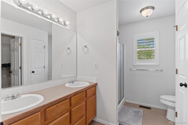 bathroom with a stall shower, toilet, double vanity, baseboards, and a closet