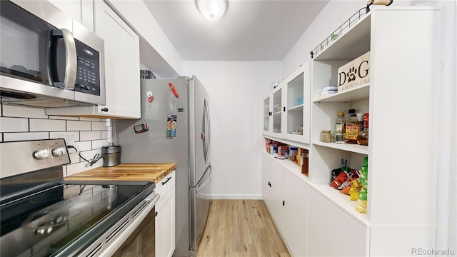 kitchen featuring butcher block countertops, tasteful backsplash, light wood-type flooring, appliances with stainless steel finishes, and white cabinets