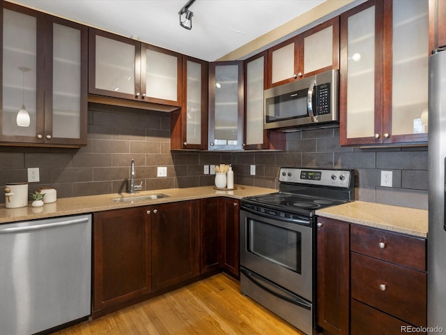 kitchen with light stone countertops, appliances with stainless steel finishes, sink, light wood-type flooring, and backsplash