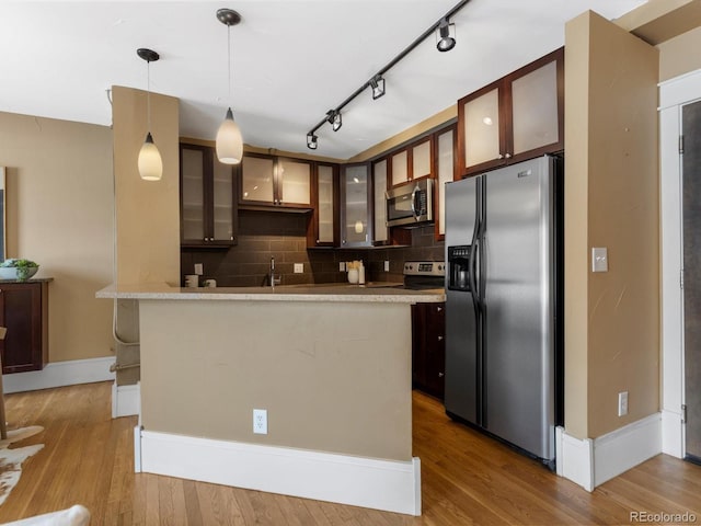 kitchen with wood finished floors, stainless steel appliances, glass insert cabinets, decorative light fixtures, and backsplash