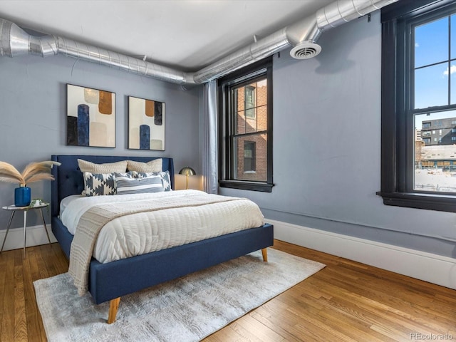 bedroom with wood finished floors, visible vents, and baseboards